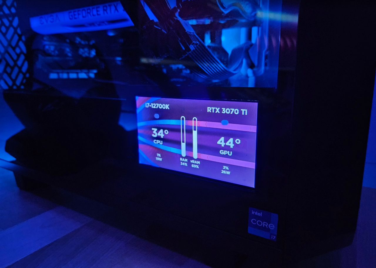 The SystemHUD screen glowing pink and blue in the bottom corner of a dark gaming PC, showing an i7-12700K at 34 degrees and an RTX 3070 Ti at 44 degrees.